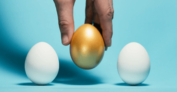 A hand picks up a golden egg from in between two white eggs.
